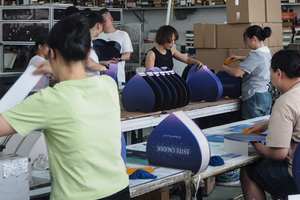 Team of workers assembling heart-shaped custom packaging boxes in a production line.