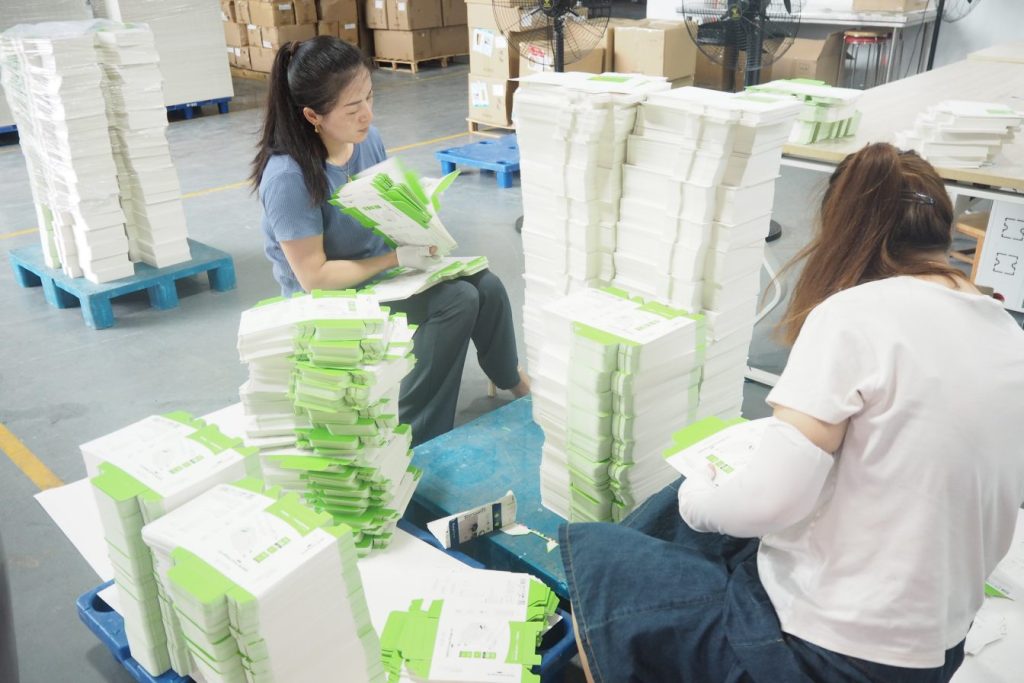 Workers inspecting and stacking packaging boxes for quality assurance.