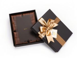 Black and gold chocolate gift box with a satin ribbon, showcasing premium chocolate pieces inside.
